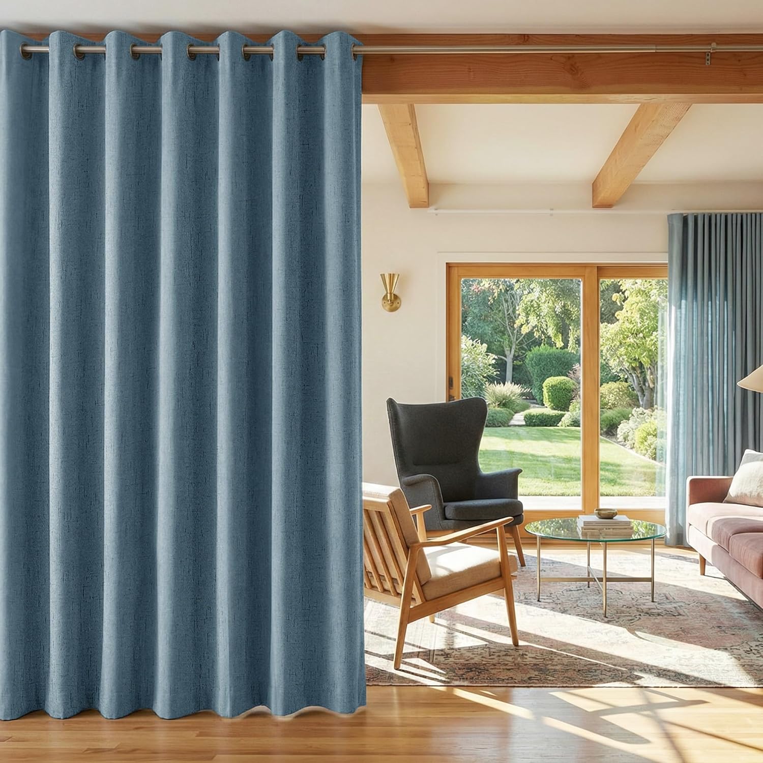 Full length slate blue textured grommet top curtain used as a room divider in a bright living space.