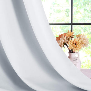 Smooth white blackout curtain panel draped elegantly by a window, with soft folds highlighting its thick fabric.