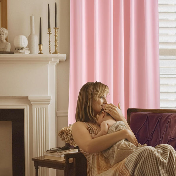 Soft pink blackout curtains hanging by a window in a cozy nursery scene with a mother holding a baby.