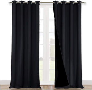 Solid black blackout curtains with silver grommet tops hanging on a rod in front of a white window.