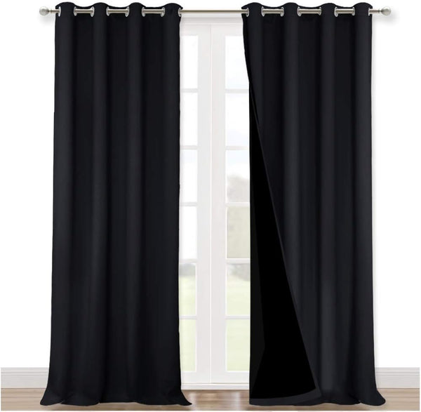 Solid black blackout curtains with silver grommet tops hanging on a rod in front of a white window.