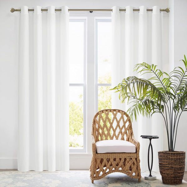 Solid white curtain panel with bronze grommet top, hanging on a metal rod over a window in a bright room.