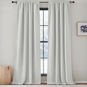 Solid white rod pocket blackout curtains hanging on a black rod over a window.