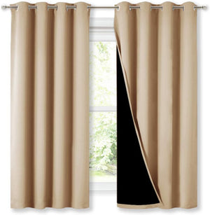 Tan blackout curtains with silver grommet tops hang on a window, revealing opaque black lining.