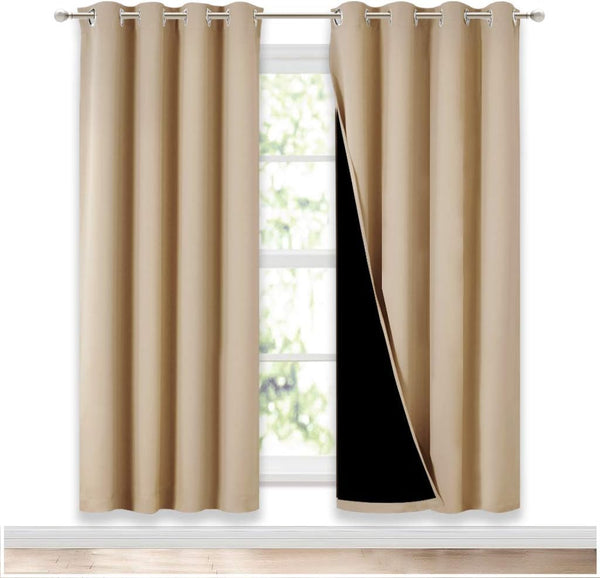 Pair of tan blackout curtains with grommet tops hanging on a silver rod, one panel revealing black lining.