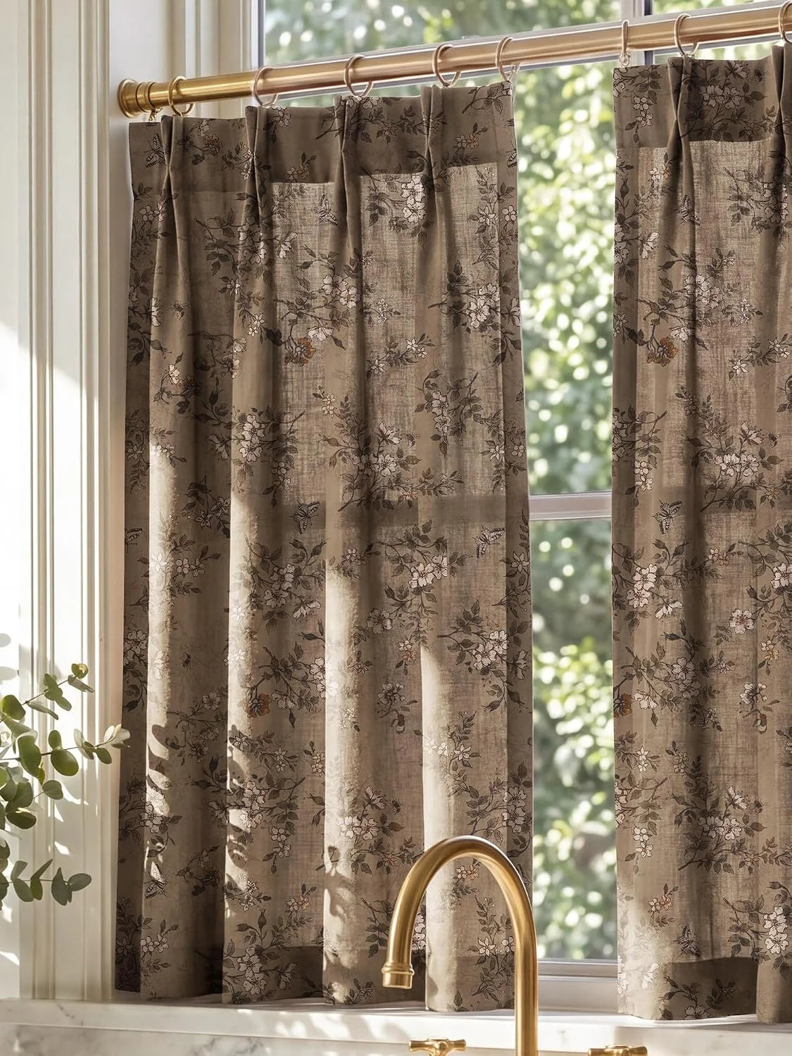 Taupe floral cafe curtains on brass rings hanging in a bright kitchen window