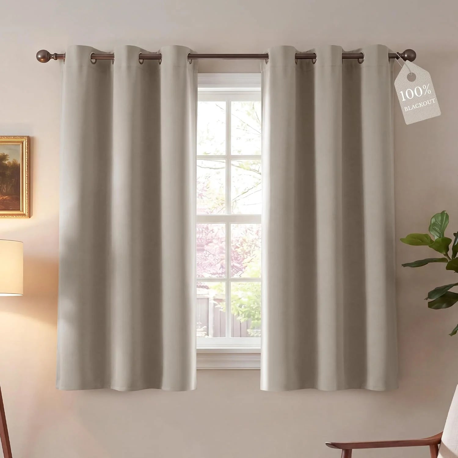 Pair of light taupe 100% blackout grommet curtains on a window rod in a cozy room.