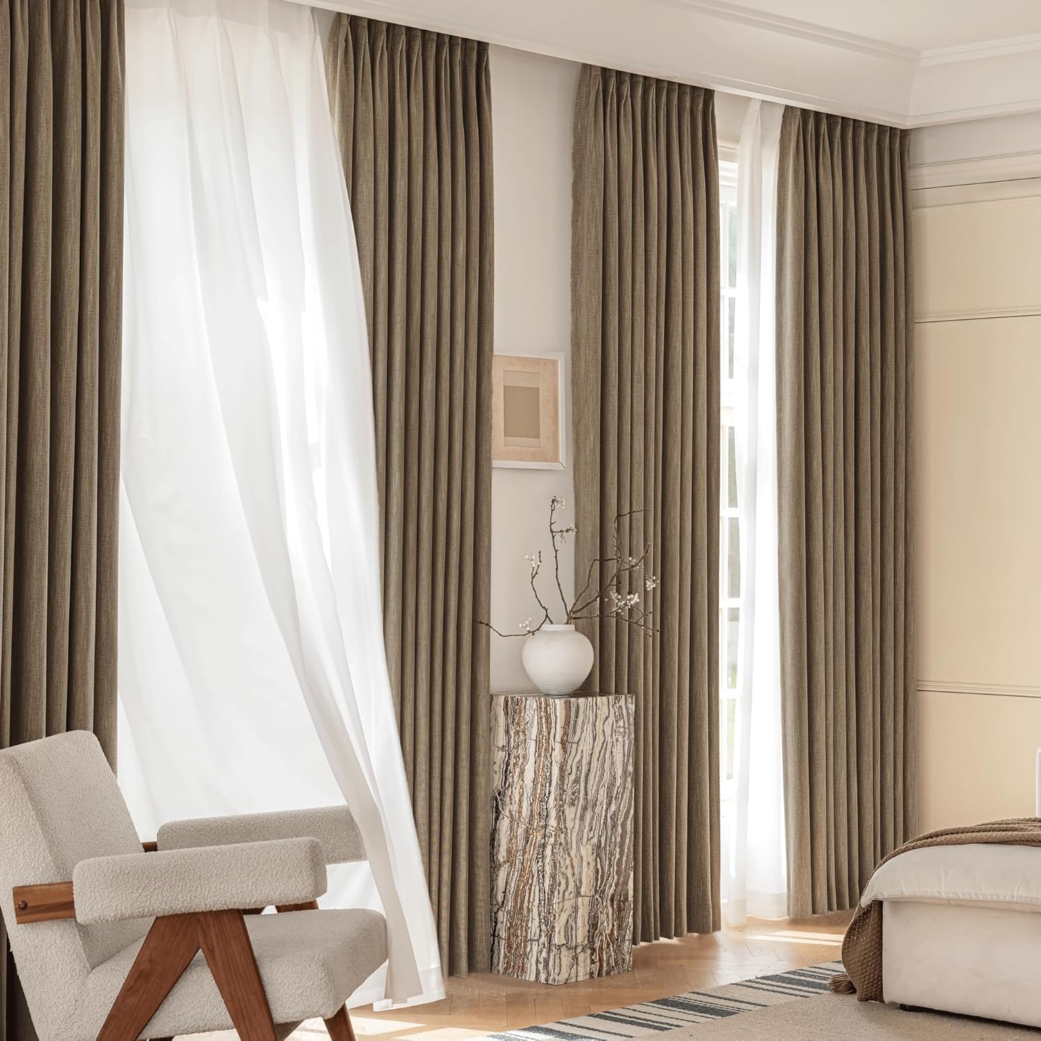 Taupe linen-look pinch pleat drapes layered with flowing white sheer curtains in a modern bedroom.
