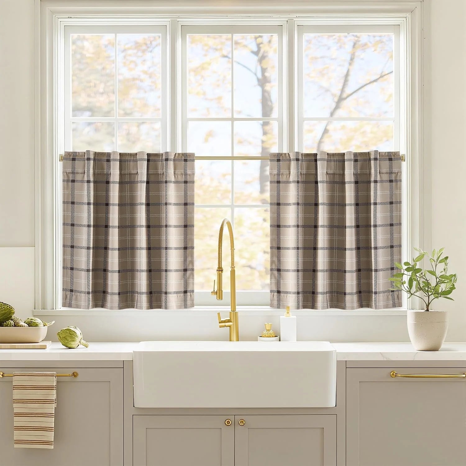 Taupe plaid cafe curtains on a brass rod above a farmhouse kitchen sink window