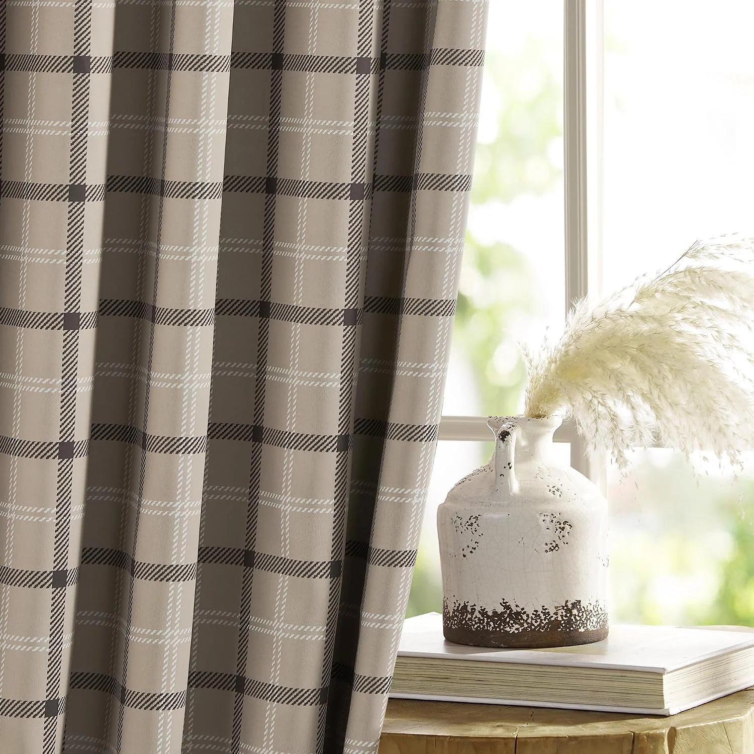 Taupe plaid curtain panel beside a bright window with rustic ceramic vase