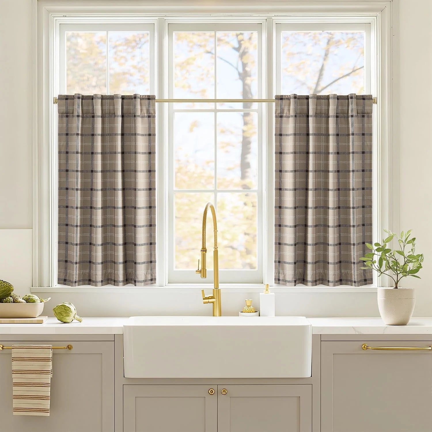 Taupe plaid tier curtains over a white kitchen sink with brass faucet