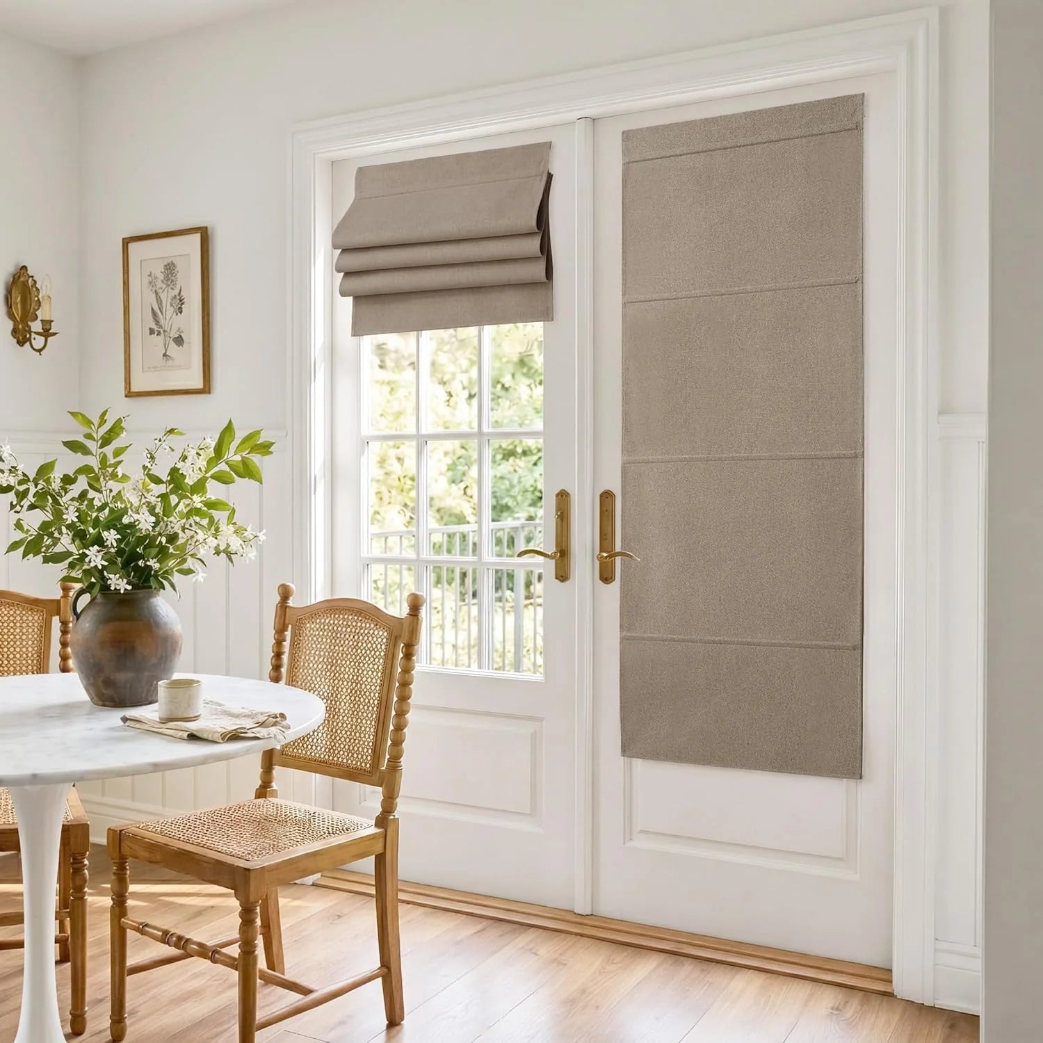 Taupe flat-fold Roman shades on white French doors in a bright dining room with a marble table and cane chairs.