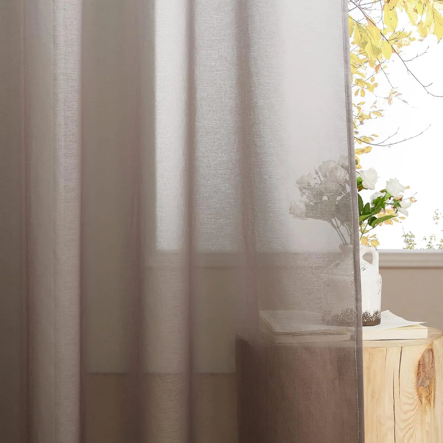 Taupe sheer linen-look curtain filtering light beside a rustic wood side table