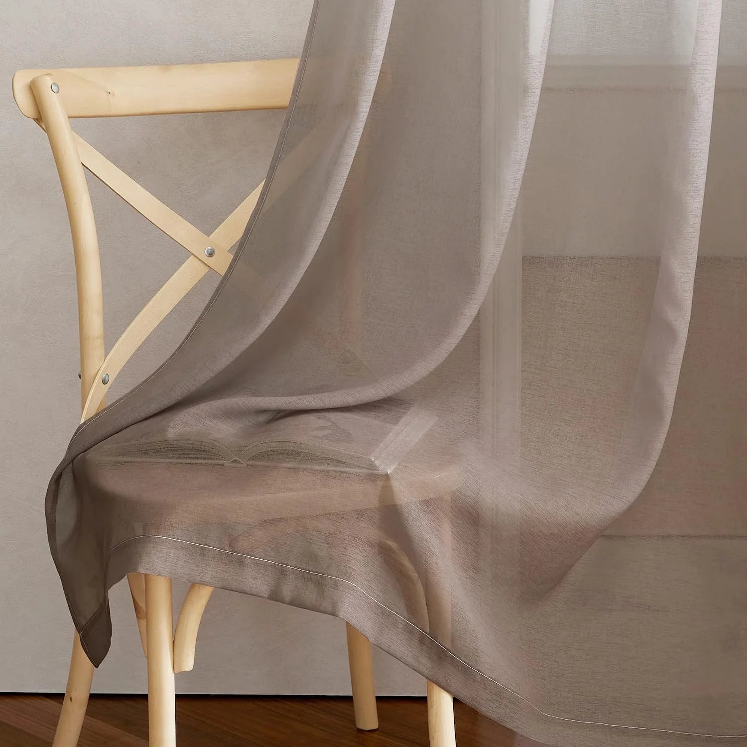 Taupe sheer voile curtain draped over a light wood chair with soft transparency