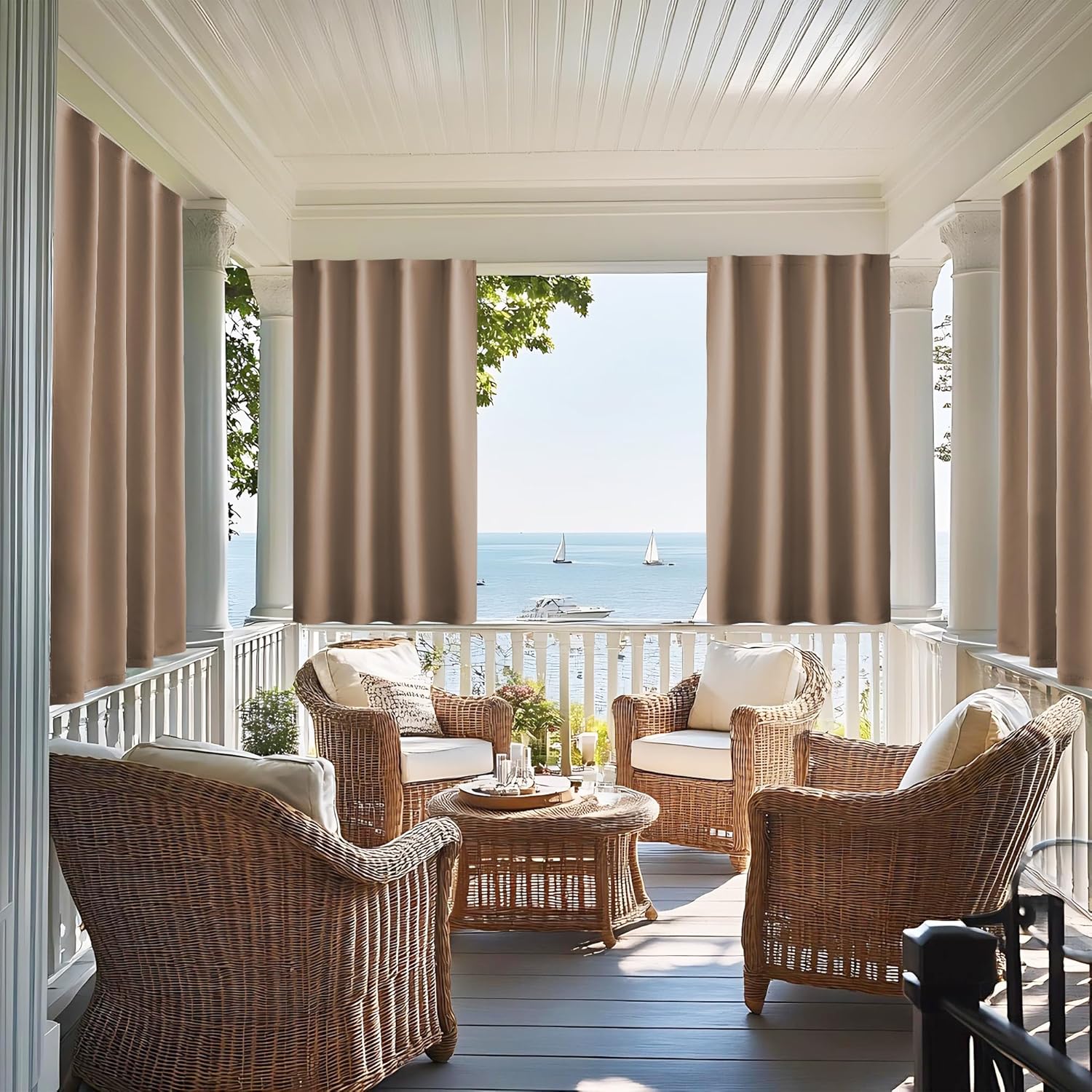 Taupe solid outdoor curtains hanging on a white porch with wicker furniture and an ocean view.