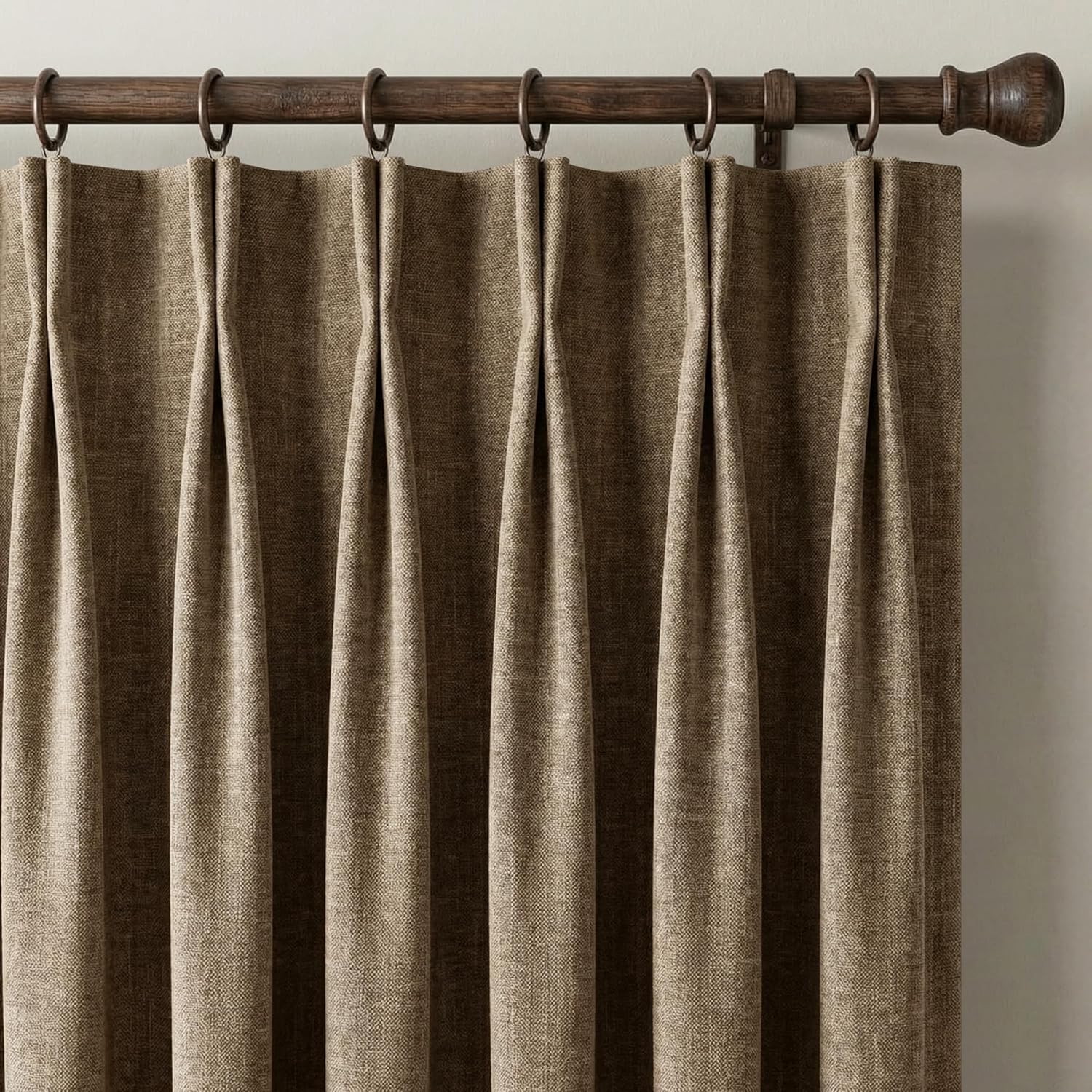 Taupe textured pinch pleat curtains hanging from a dark wood curtain rod with metal rings.