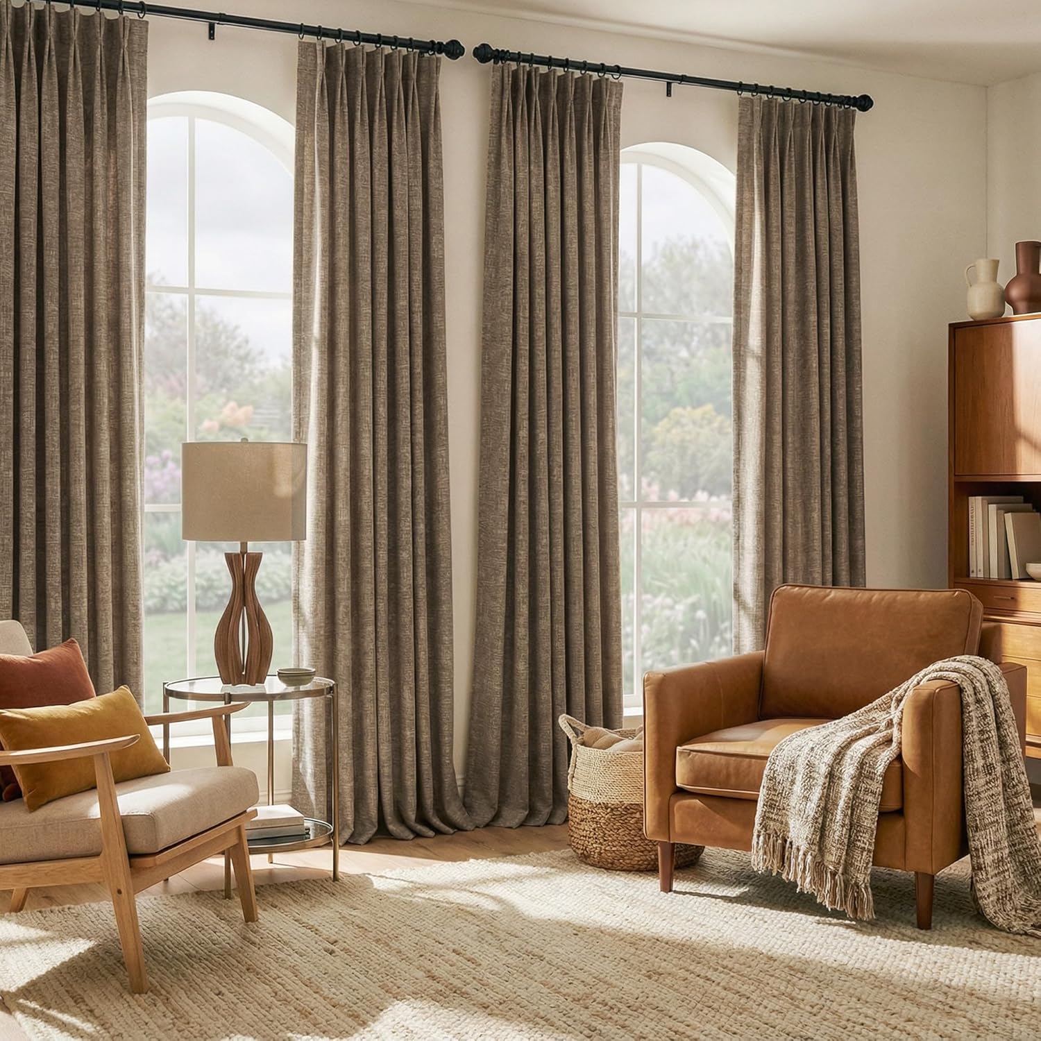 Full-length taupe textured pinch pleat drapes on a black rod covering arched living room windows.