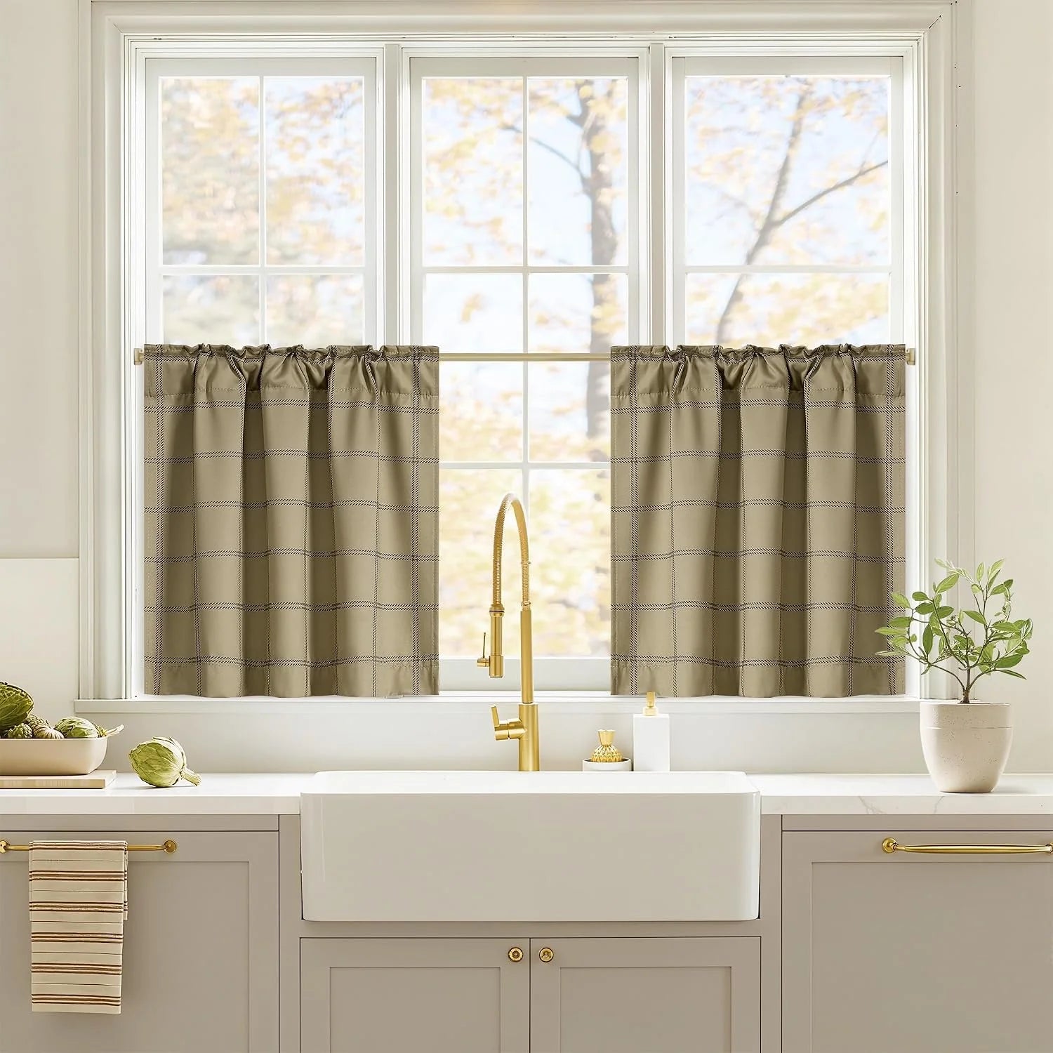 Taupe windowpane tier curtains over a white farmhouse kitchen sink and brass faucet