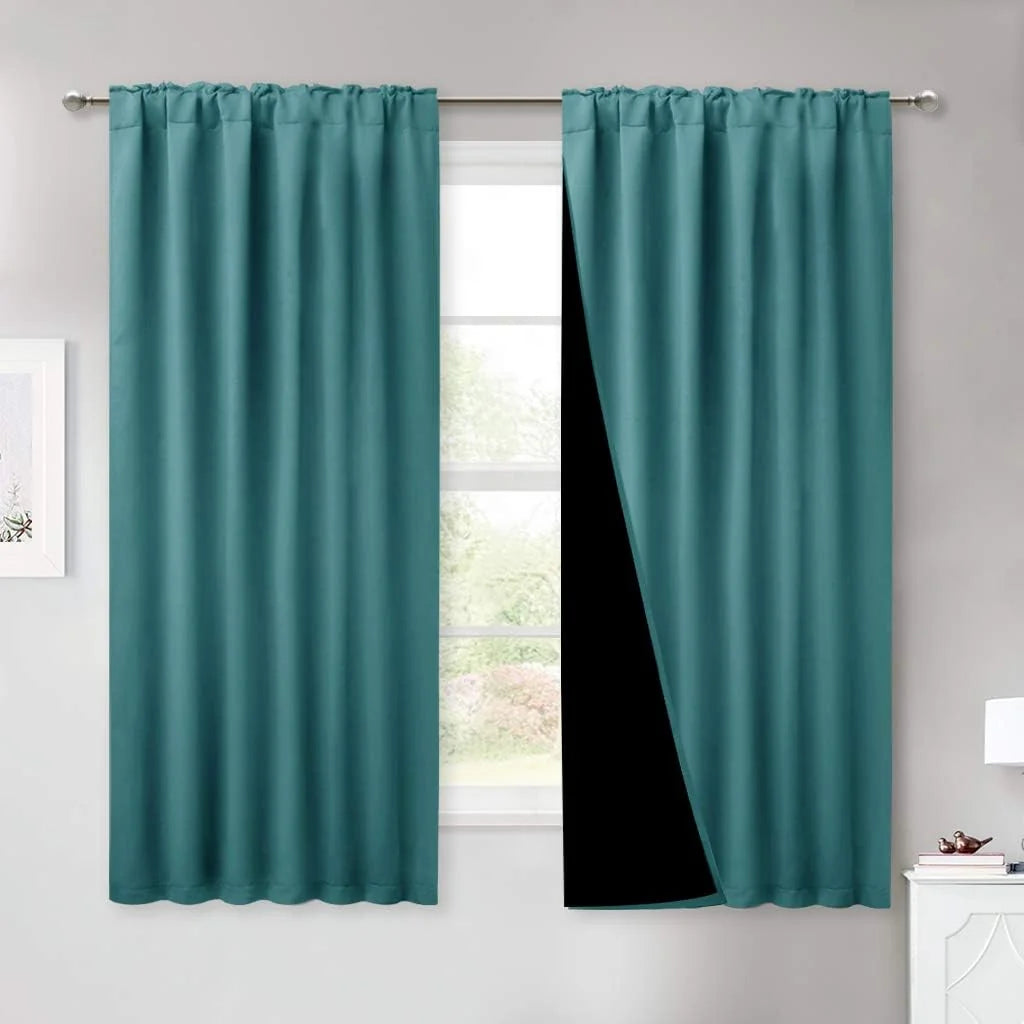 Teal blackout curtains with rod pocket top hanging on a silver rod in a bright room
