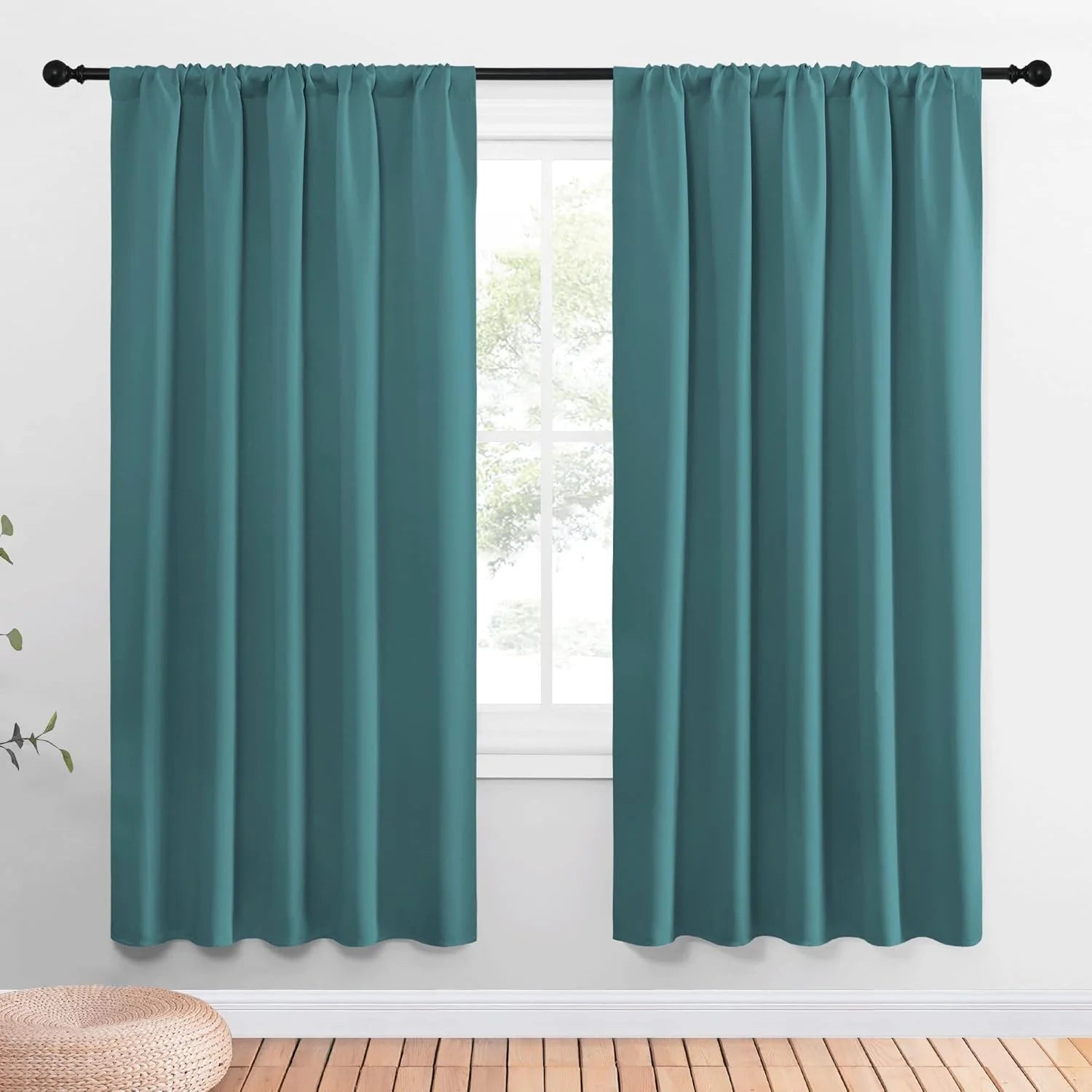 Teal rod pocket curtains hanging on a black curtain rod over a bright window
