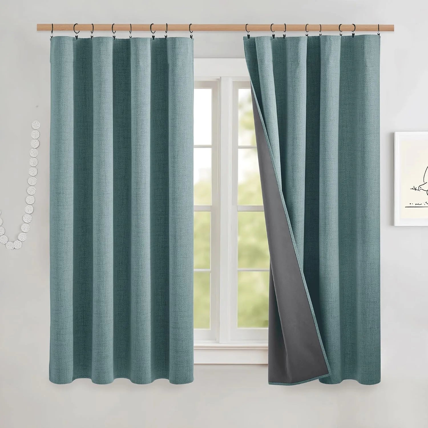 Teal linen-look blackout curtains with ring hooks on a wood rod over a bright window