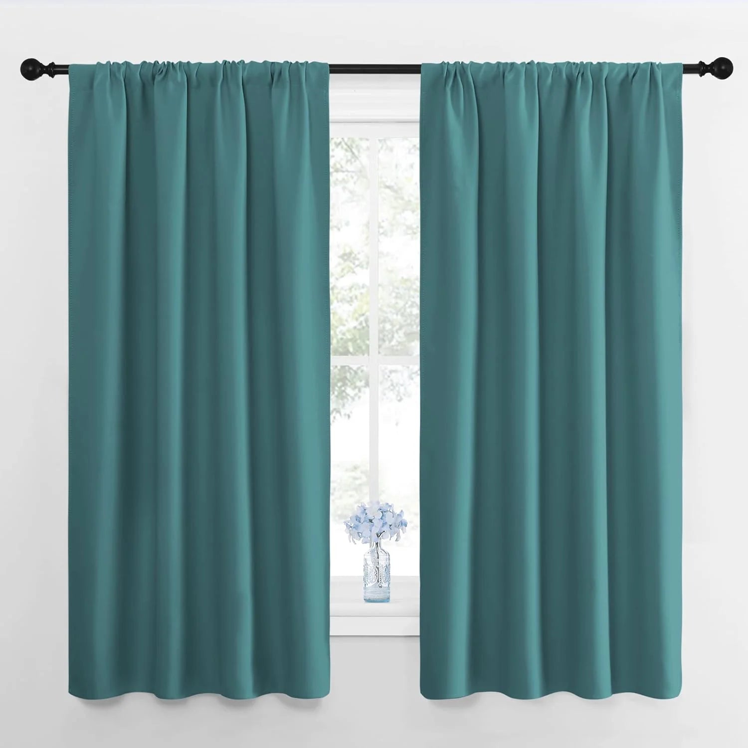 Pair of teal solid rod pocket curtains hanging on a black rod over a window.