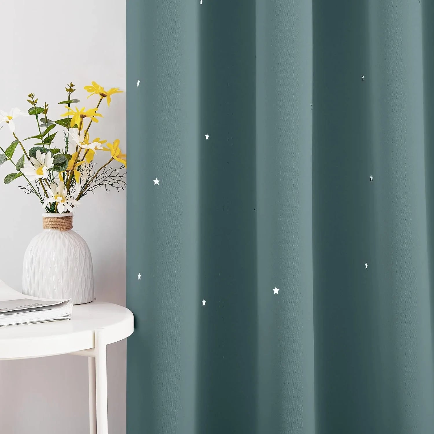 Teal curtain panel with small white star print beside a white table and flower vase