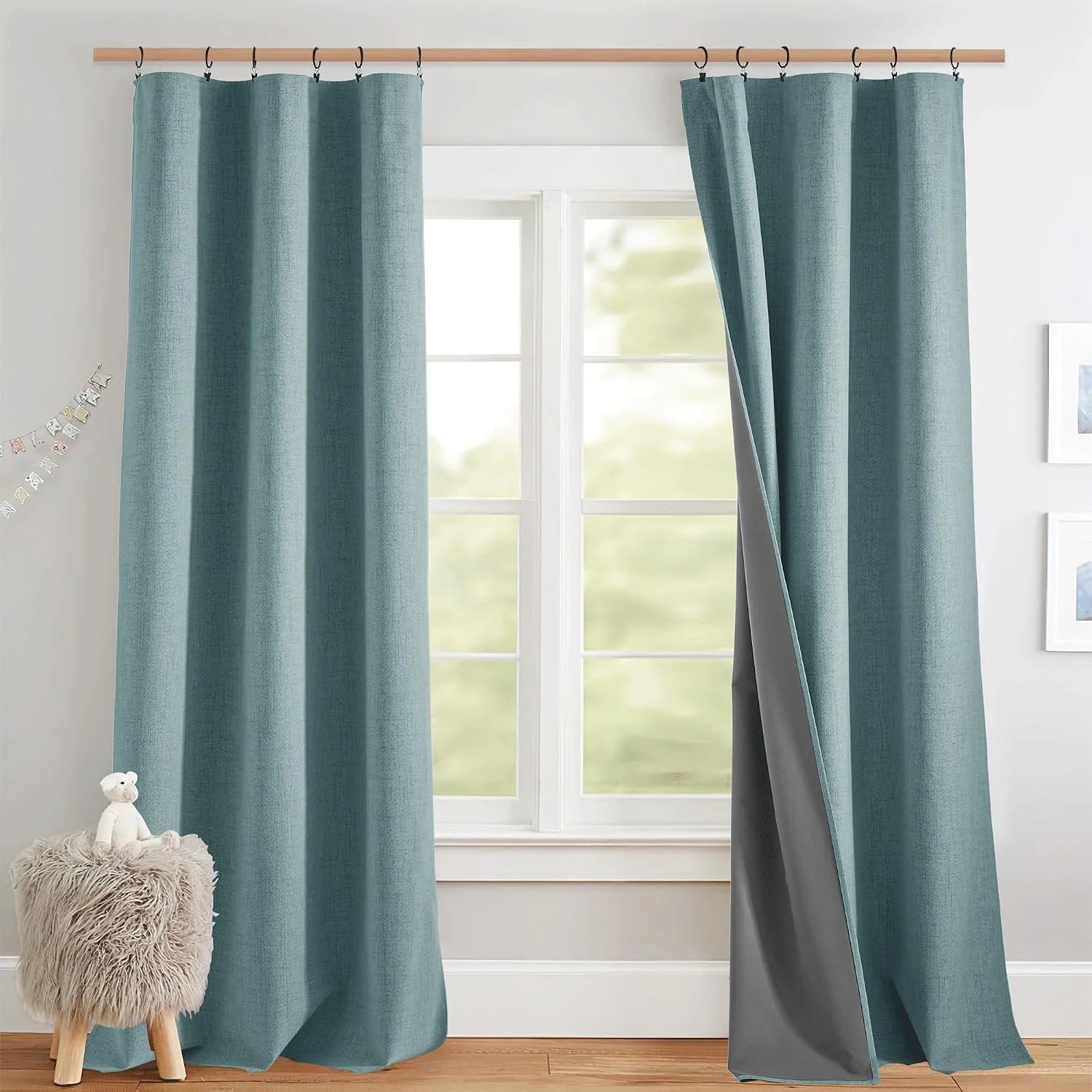 Teal textured blackout curtains on black rings over a white window in a cozy nursery