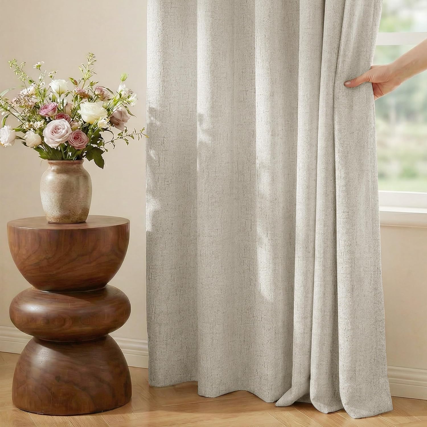 Textured light beige curtains with a visible weave. A hand pulls one panel open to reveal a window.
