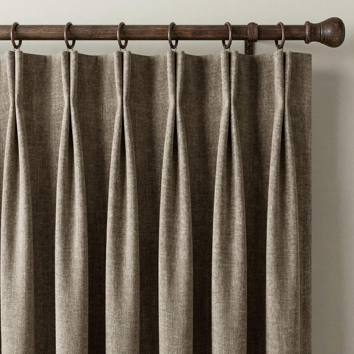 Textured taupe pinch pleat curtains hang from a dark wood rod with bronze rings.
