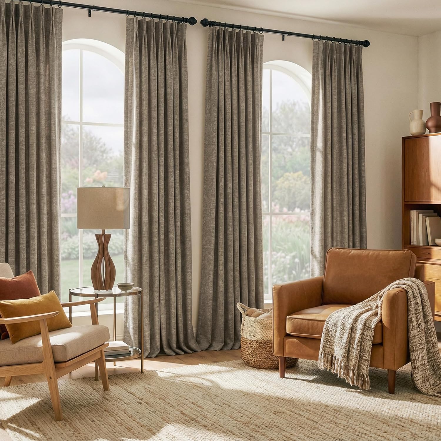 Textured taupe pleated drapes hang on black rods over three arched windows in a sunlit living room.