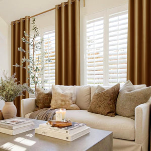 Floor-length warm bronze grommet top curtains frame a window with white shutters in a cozy living room.