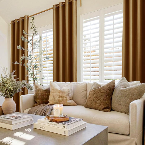 Floor-length warm bronze grommet top curtains frame a window with white shutters in a cozy living room.