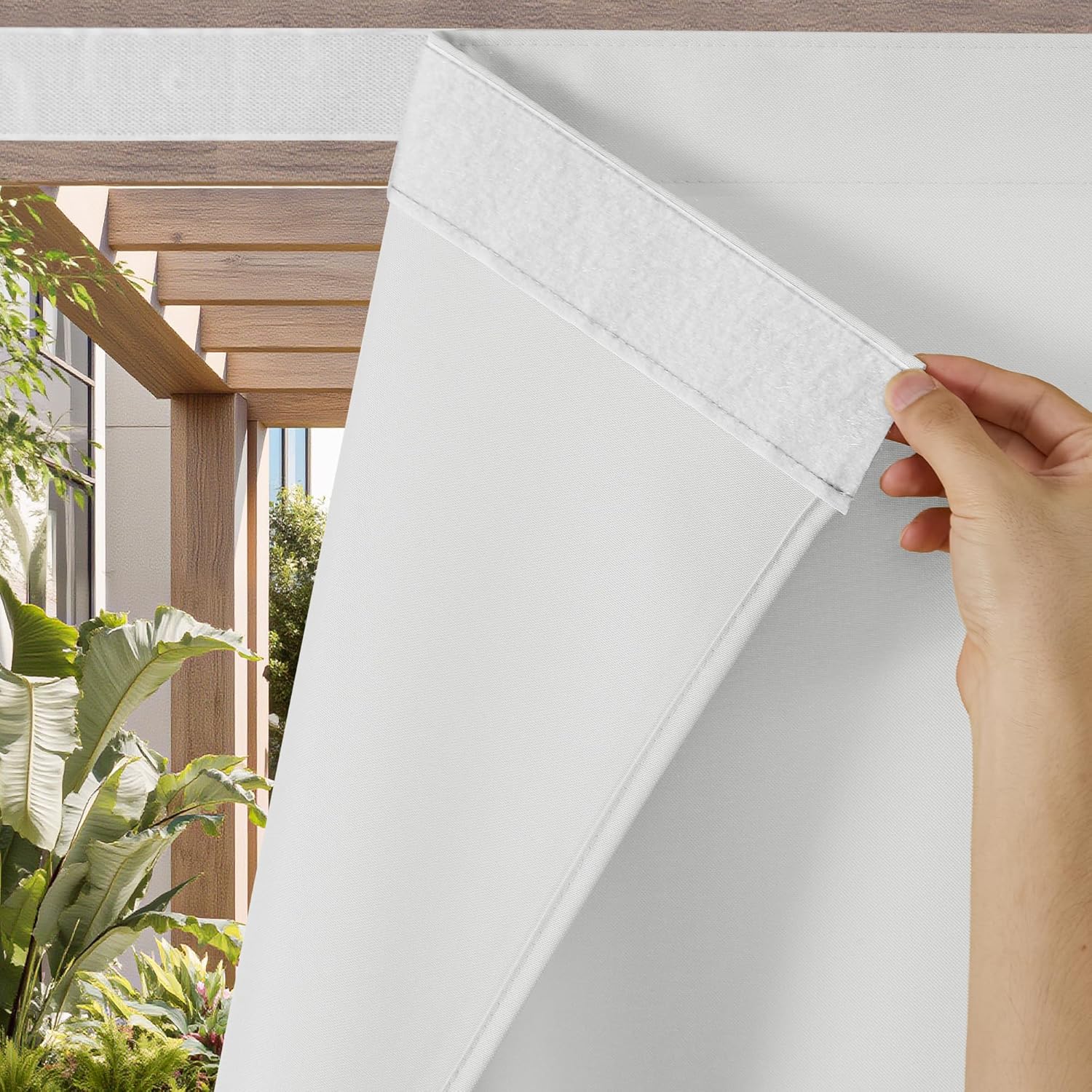 Hand reveals velcro on white outdoor patio pergola shade, with green plants visible.