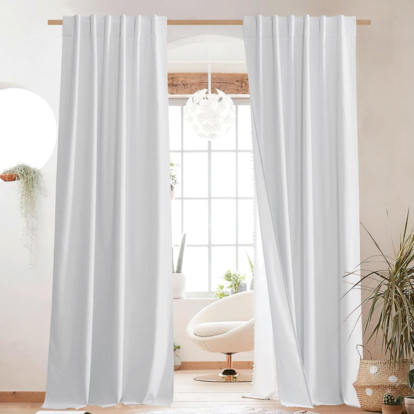 Pair of crisp white back tab curtains hanging on a wooden rod, framing a bright window in a modern room.