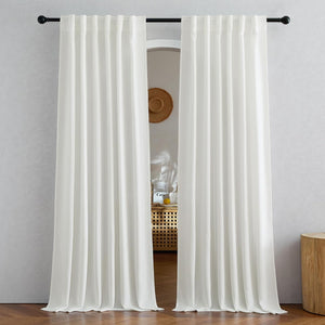 Two white back tab window curtain panels elegantly draped on a black rod, touching a wooden floor.