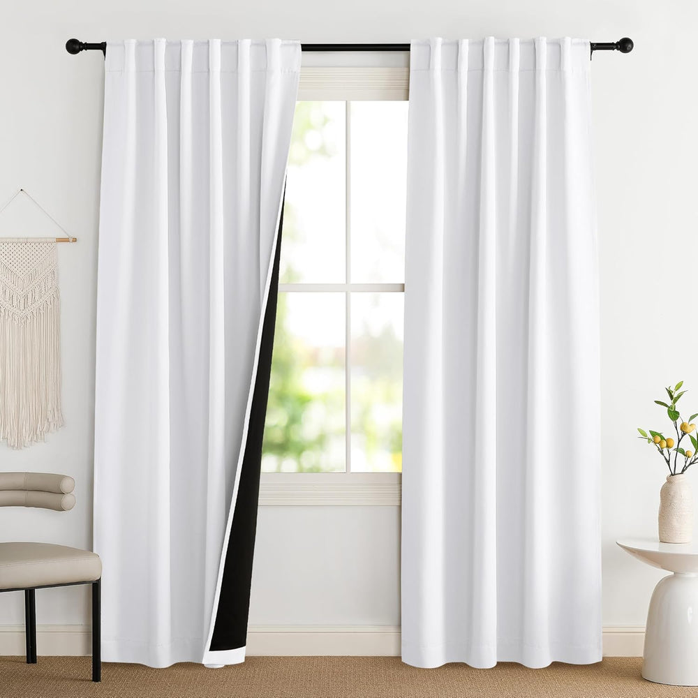 Two white blackout back tab curtains hanging on a black rod in a bright room, one curtain pulled back revealing black lining.