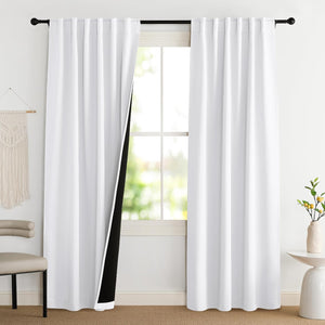 Two white blackout back tab curtains hanging on a black rod in a bright room, one curtain pulled back revealing black lining.