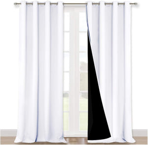 White blackout curtains with silver grommet tops hang over a window. The right panel reveals its black lining.