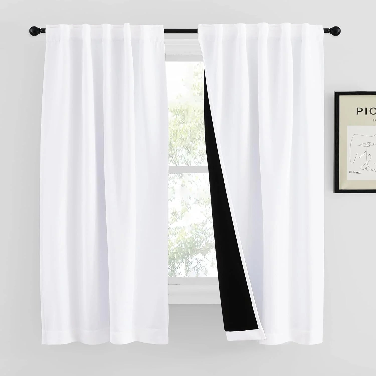 White rod pocket blackout curtains on a black curtain rod by a bright window