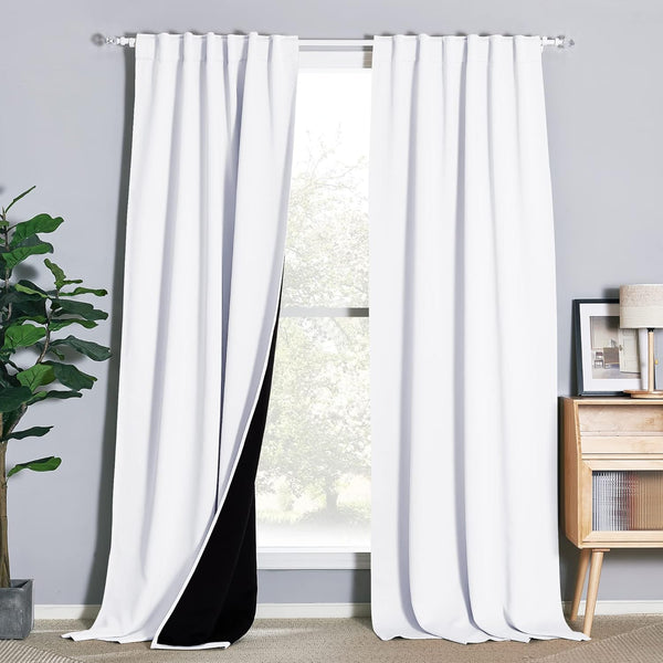 White blackout curtains with black lining and rod pocket top hanging on a window in a modern room setting.