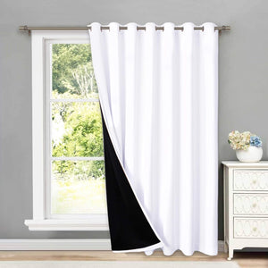 White grommet top blackout curtain panel with a black lining, hung on a silver rod over a window.