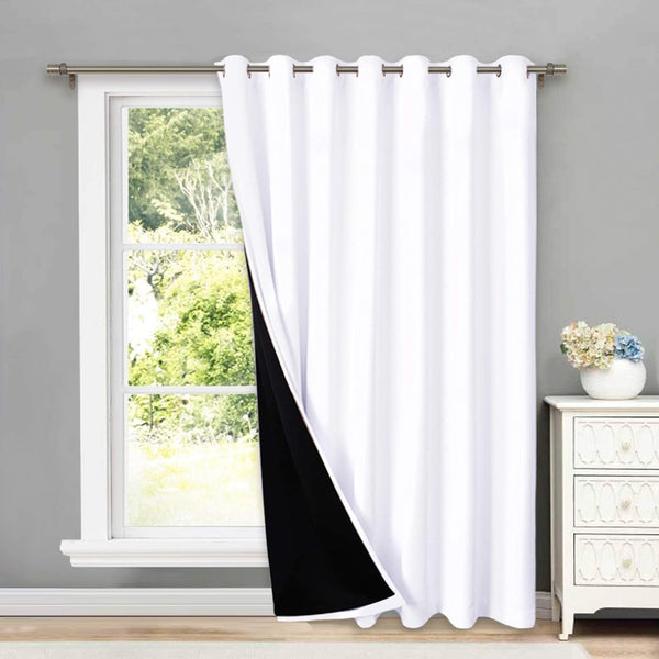 White grommet top blackout curtain panel with a black lining, hung on a silver rod over a window.
