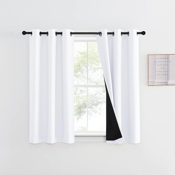 White blackout curtains with black lining and grommet top, hanging over a window.