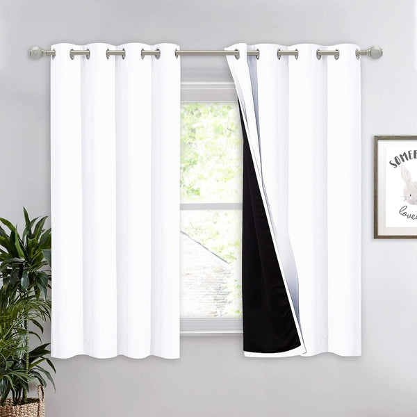 White blackout curtains with silver grommet tops on a silver rod, one panel revealing its black lining.
