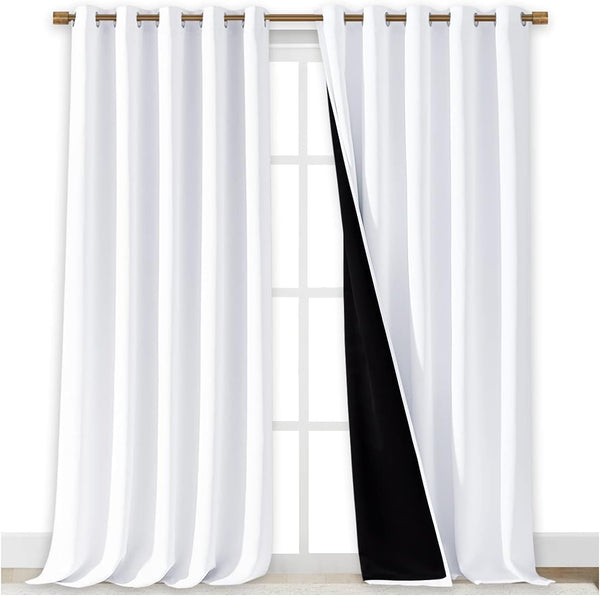 White blackout curtains with bronze grommet top hanging on a rod. Black lining is visible on the inner side of one panel.