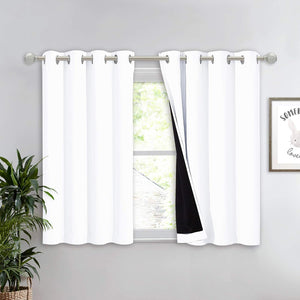 White blackout grommet top tier curtains with black lining, hanging on a silver rod over a window.