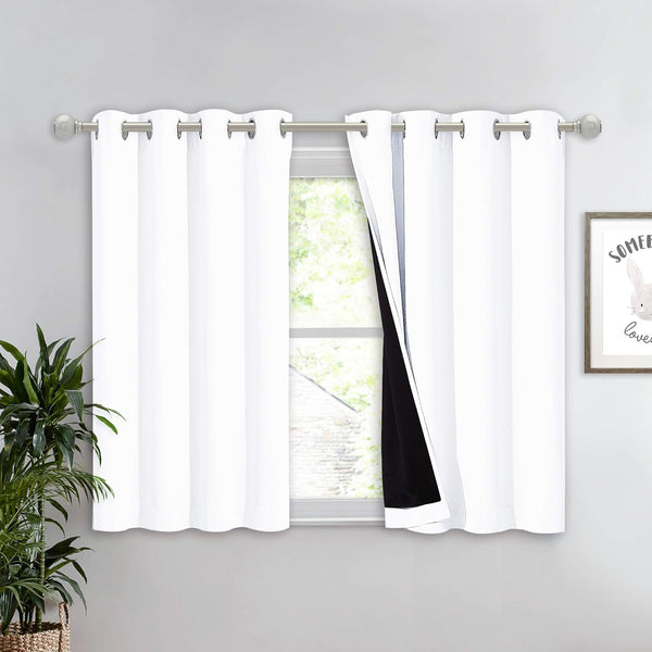 White blackout grommet top tier curtains with black lining, hanging on a silver rod over a window.