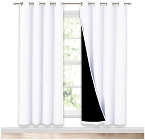 A pair of white blackout curtains with grommet tops hangs on a silver rod, one panel revealing a black lining.