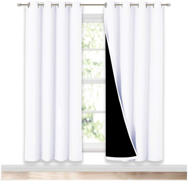 A pair of white blackout curtains with grommet tops hangs on a silver rod, one panel revealing a black lining.